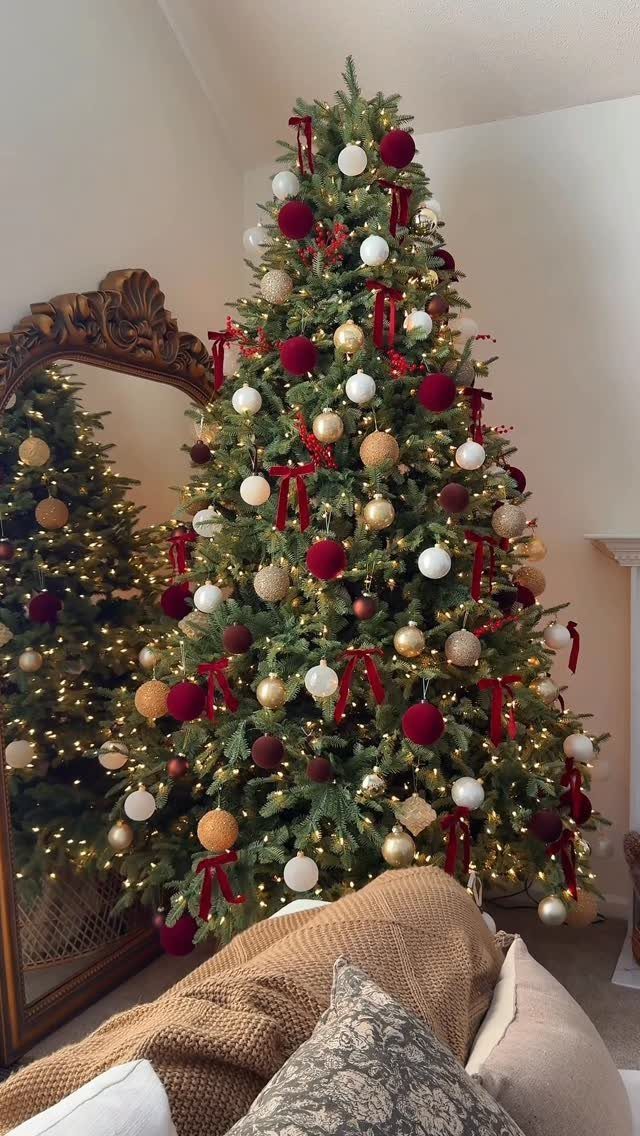 Christmas tree decorated with red velvet ribbon bows and gold and white ornaments.
