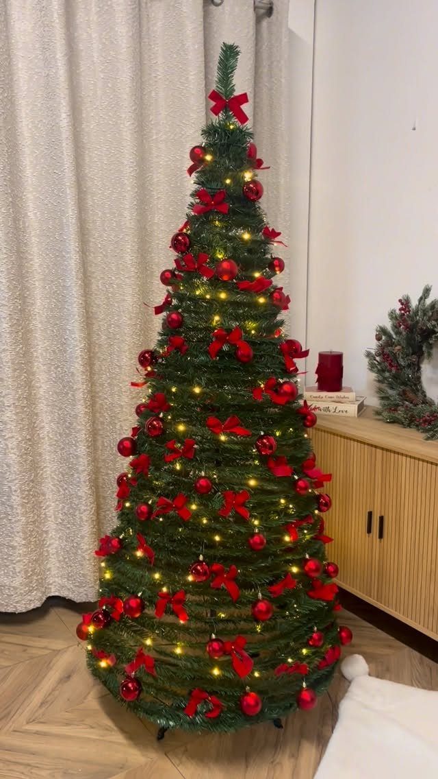 Slim green Christmas tree topped with a red ribbon bow and red ornaments.