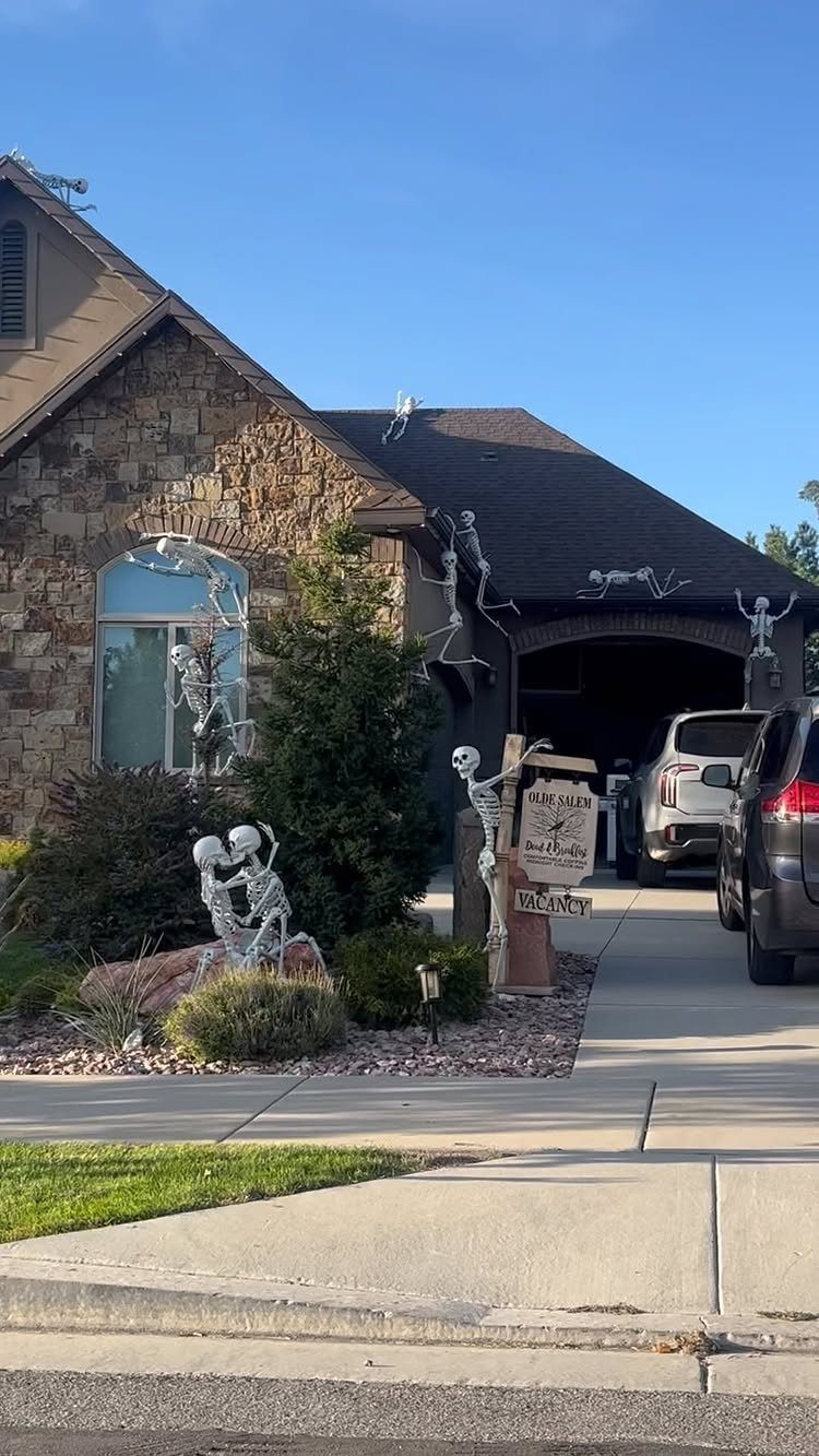 Stone house exterior decorated with multiple white plastic skeletons for Halloween