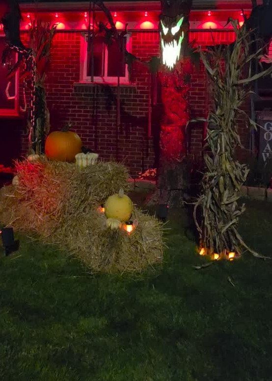 Halloween yard display with hay bales, pumpkins, and a glowing scary monster figure.