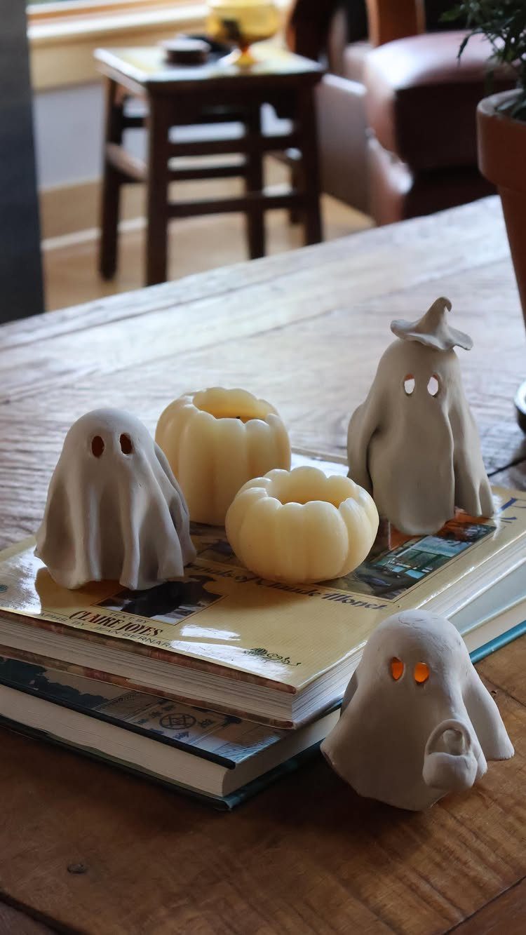 Ghost and pumpkin tea light holders with glowing orange eyes on stacked books.
