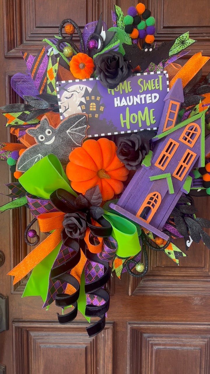 Halloween wreath on a wooden door with pumpkins, a haunted house, and ribbons.