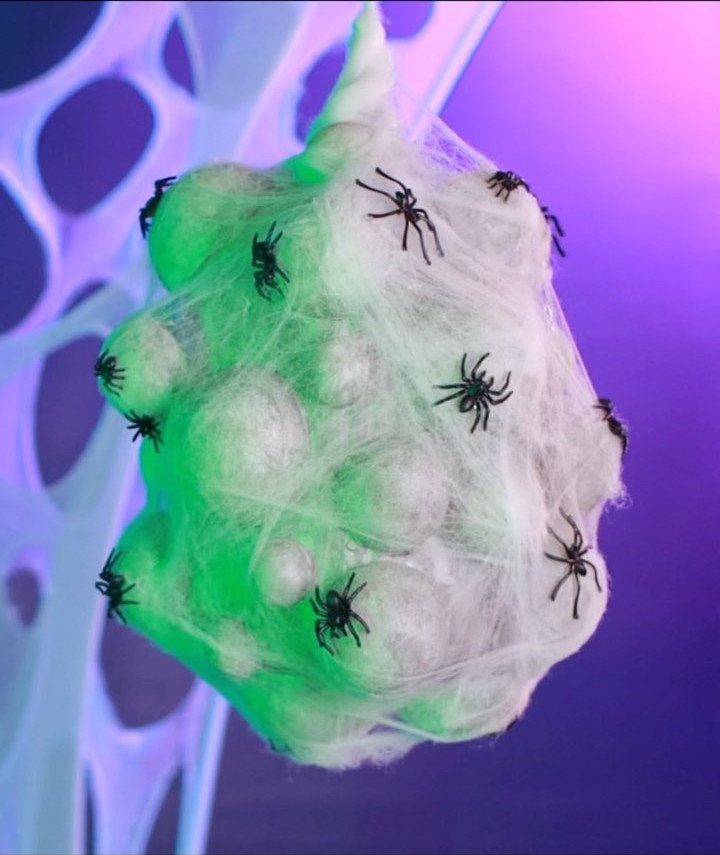 Web-like cluster with black spiders illuminated by green light against purple background
