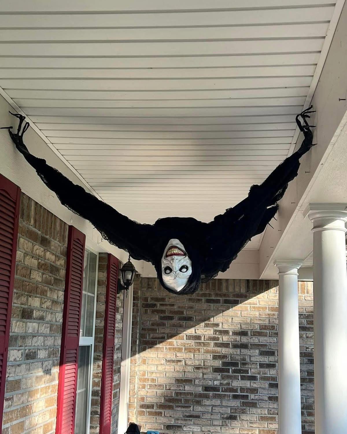 Scary black figure with a white smiling face hanging from a porch ceiling.