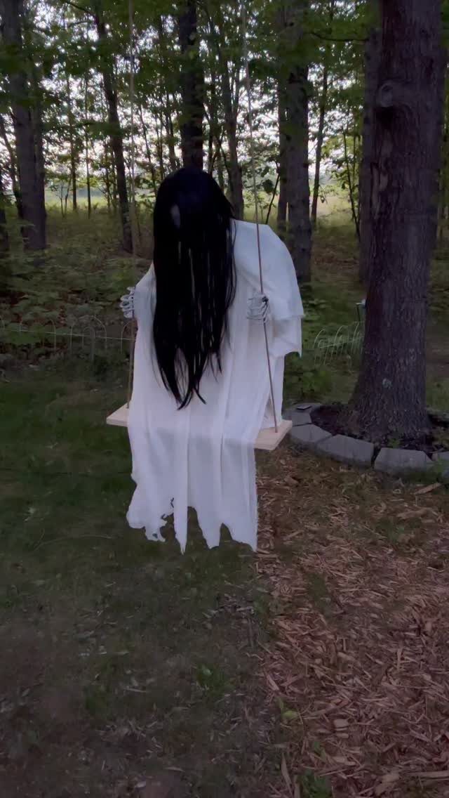 Spooky figure in white robe with long black hair sitting on a swing