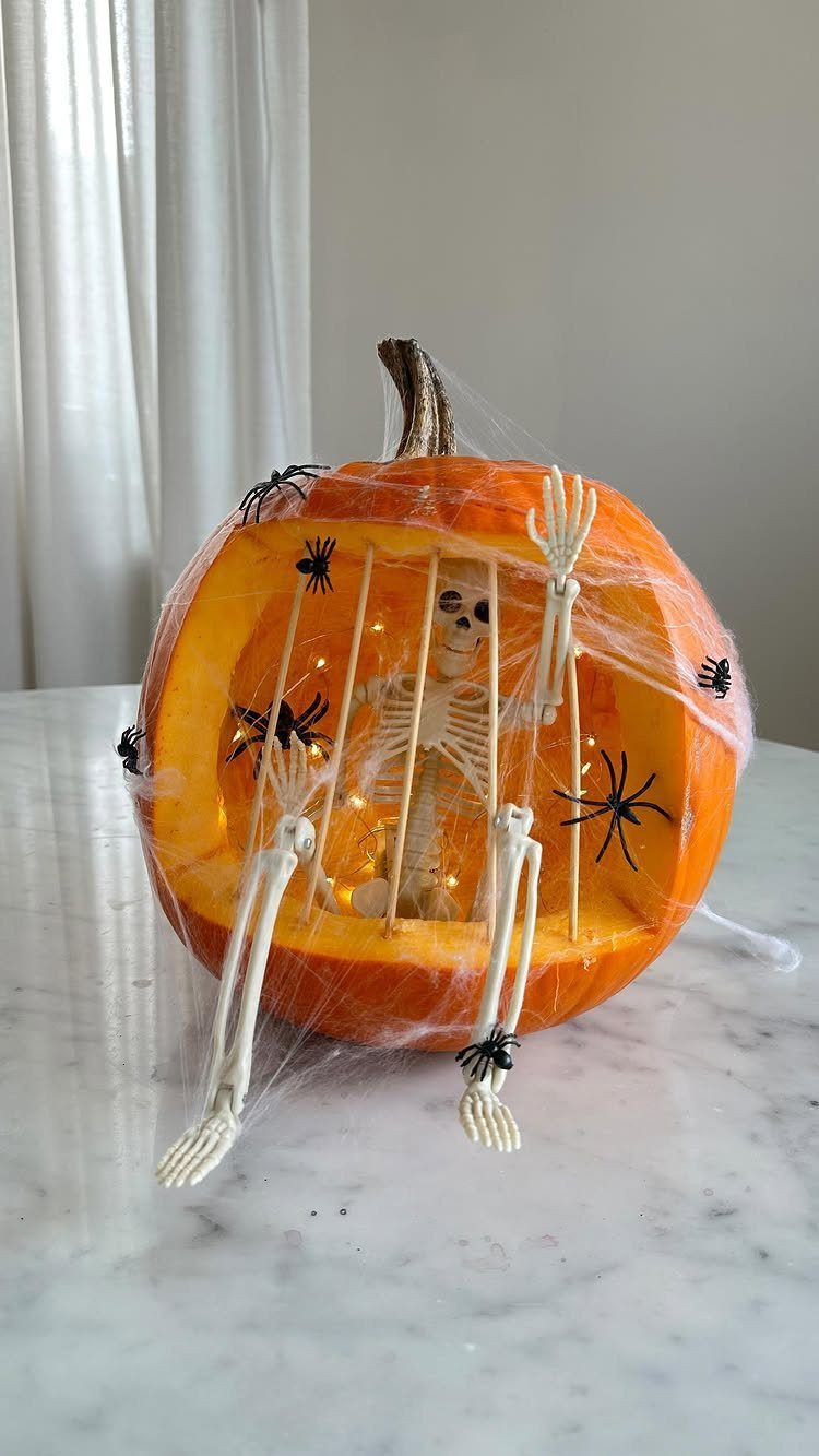 Carved pumpkin cage with a small skeleton and fairy lights inside, draped in webs.