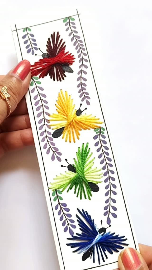 Handmade bookmark with colorful thread butterflies and purple leaf patterns on white paper.