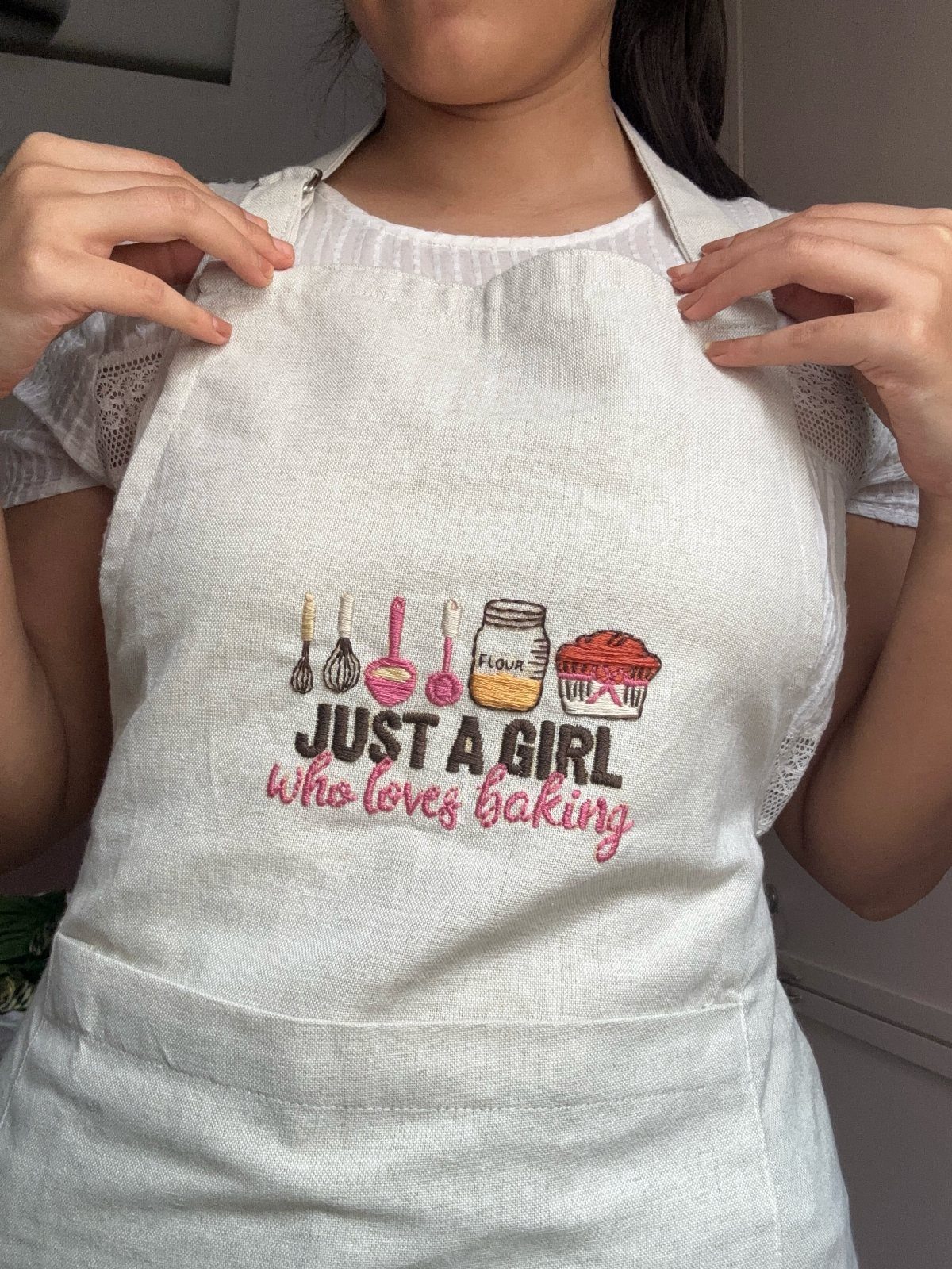 White fabric apron with baking-themed embroidery and text worn by a person.