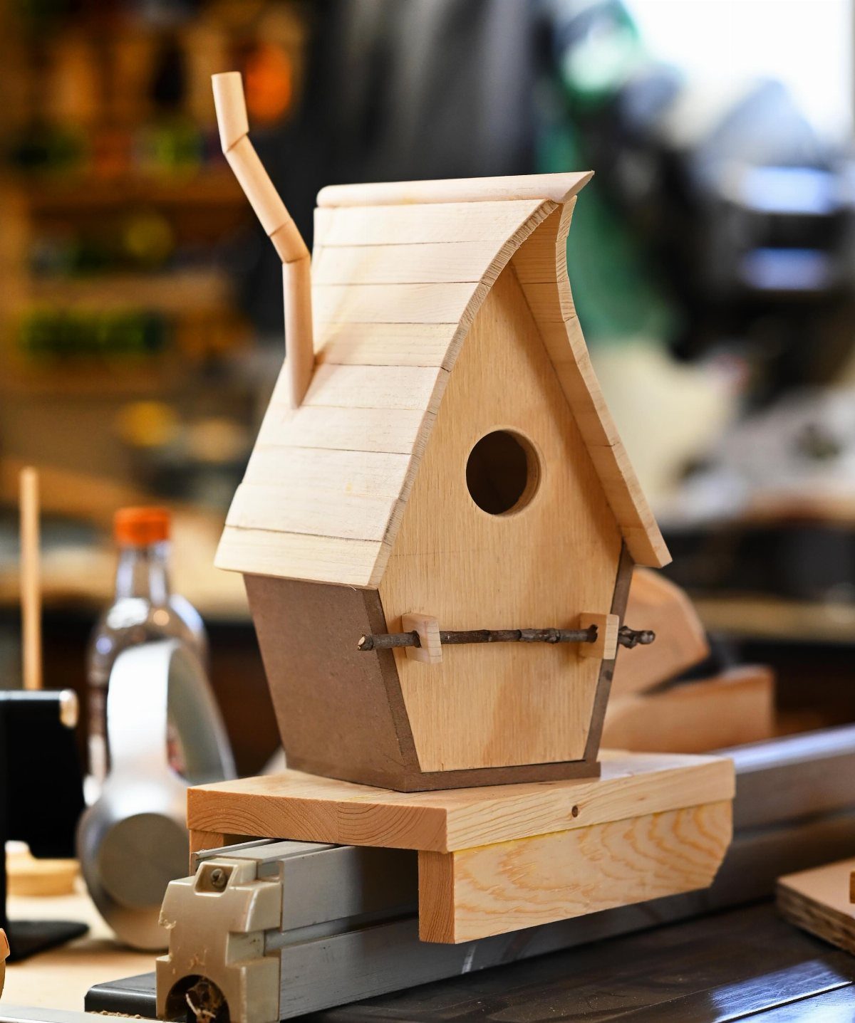 Wooden birdhouse with a curved roof sitting on a workshop workbench.