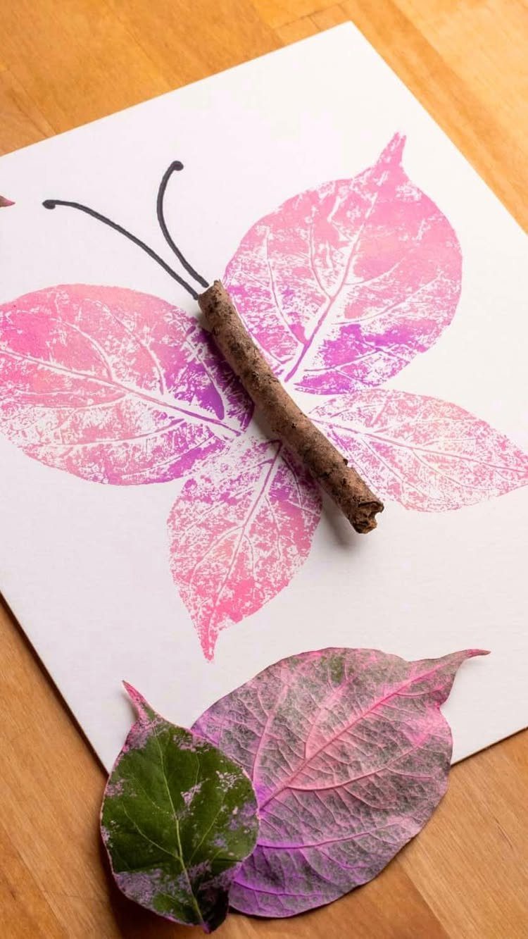 Butterfly art made from pink leaf stamps and a twig on white paper.