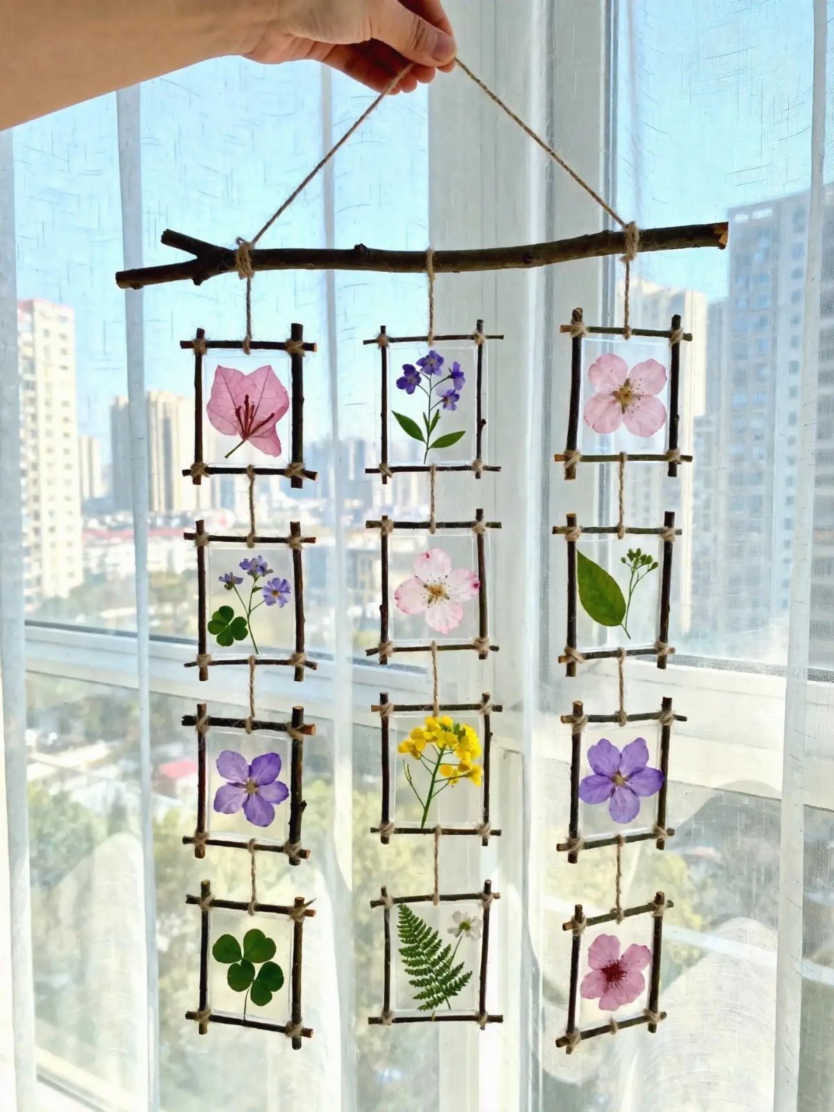 Pressed colorful flowers and leaves in small twig frames hanging from a branch.