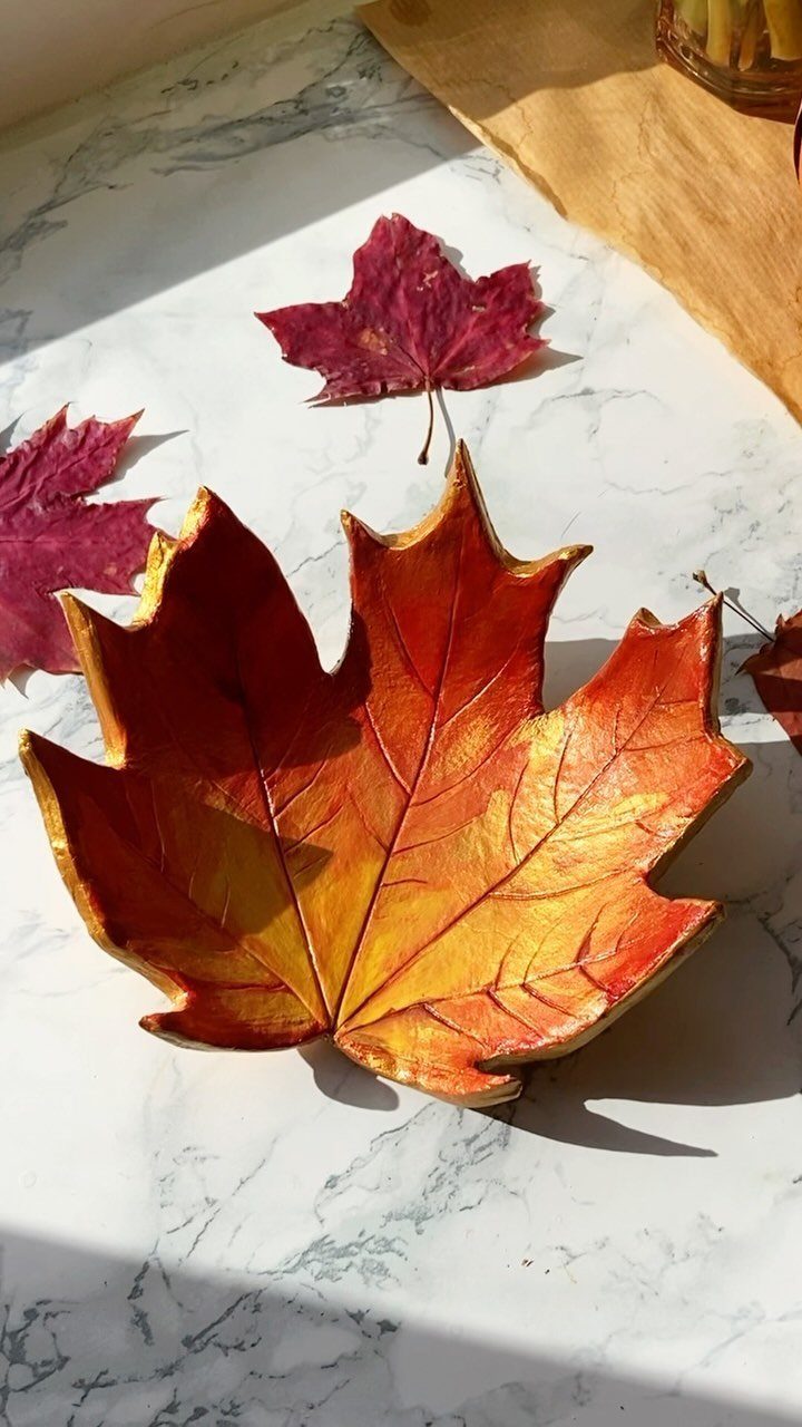 Gold and orange metallic leaf-shaped clay bowl on a white marble surface.
