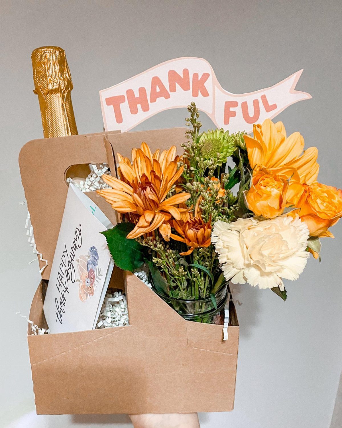 Handmade Thanksgiving hostess gift with flowers, gold bottle, and Thankful banner.