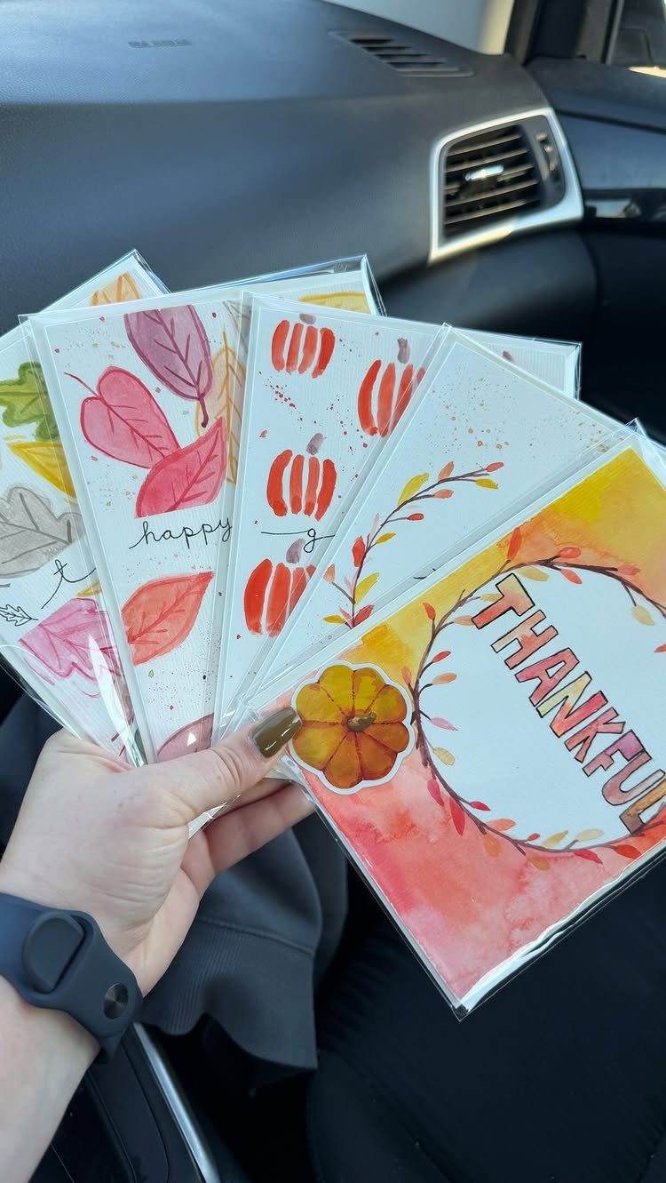 Handmade Thanksgiving greeting cards with watercolor pumpkins and autumn leaves in plastic sleeves.