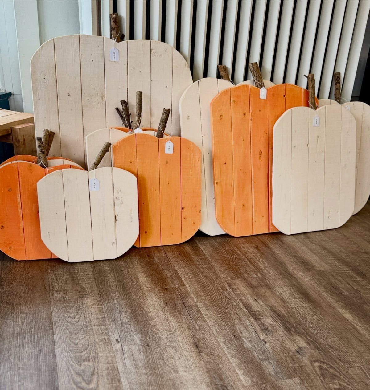Wooden pumpkin cutouts in orange and white with twig stems on wood floor