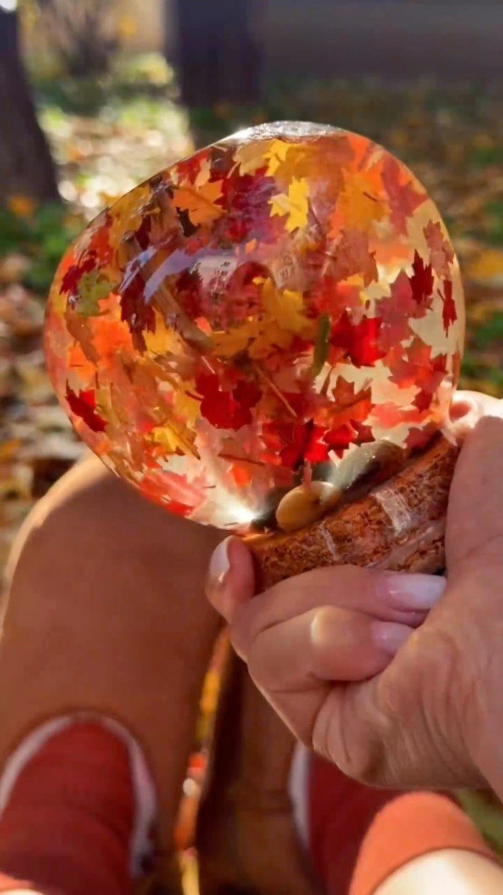 Resin sphere with colorful autumn leaves held in a hand over fall foliage