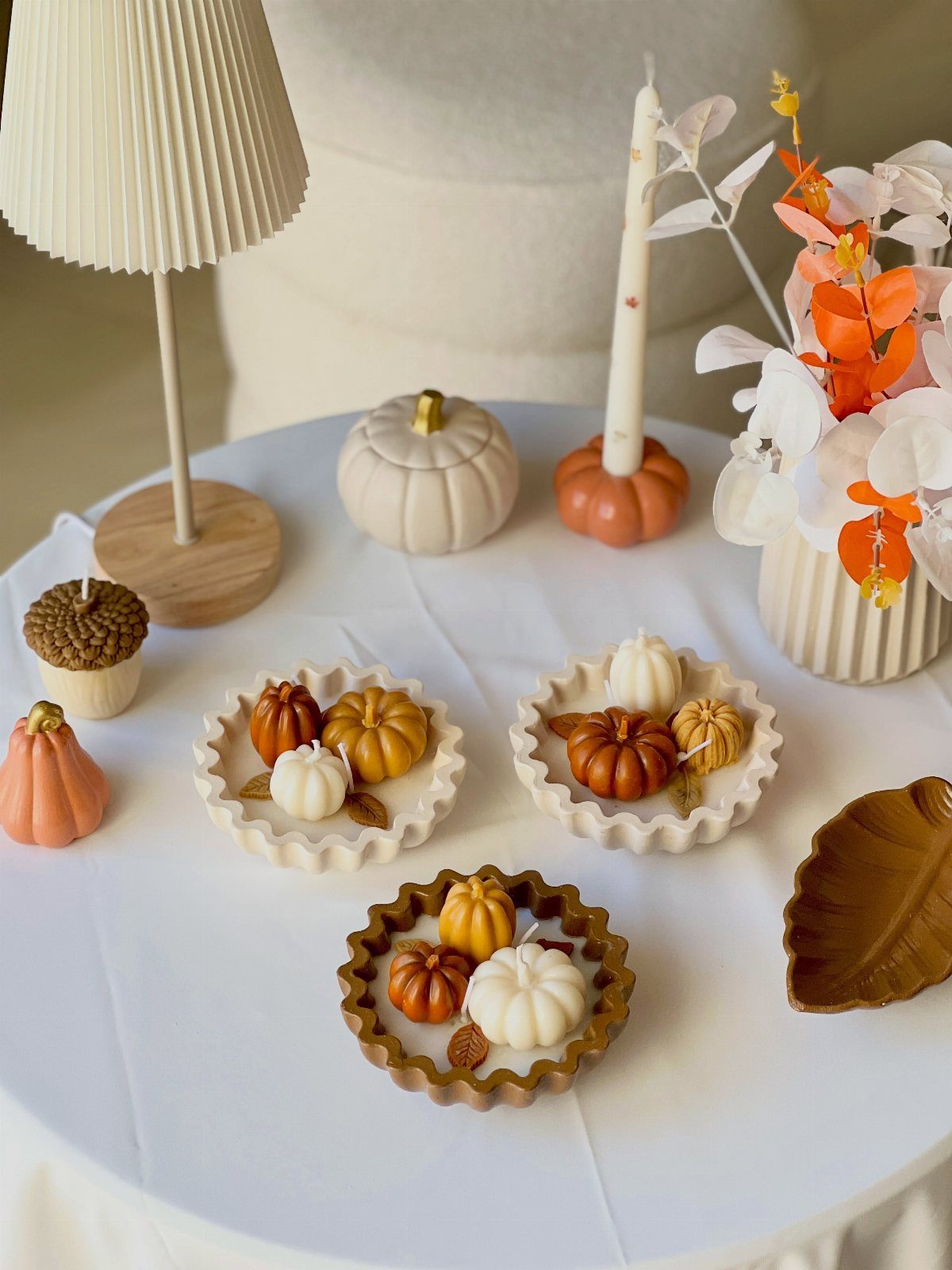 Autumn-themed table decorations with pumpkin candles, a white pumpkin, and leaf-shaped dishes.