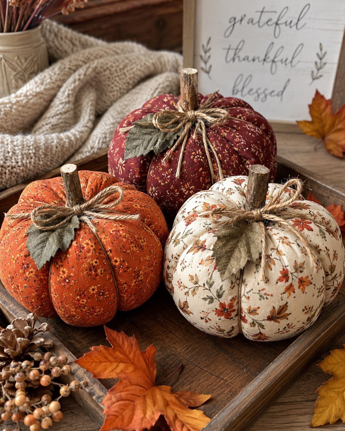 Three fabric pumpkins in autumn colors arranged on a rustic wooden tray.