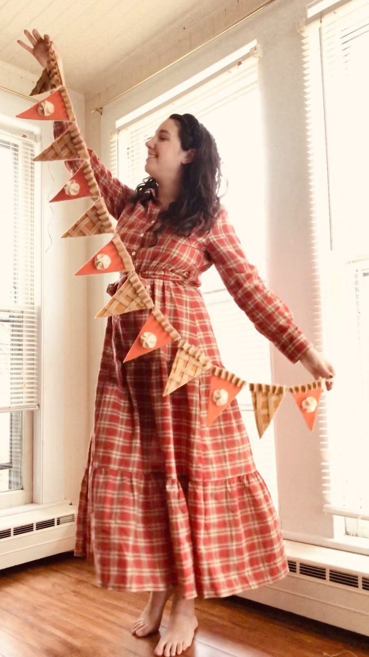 Woman holding a handmade orange and brown fabric bunting garland in a bright room.