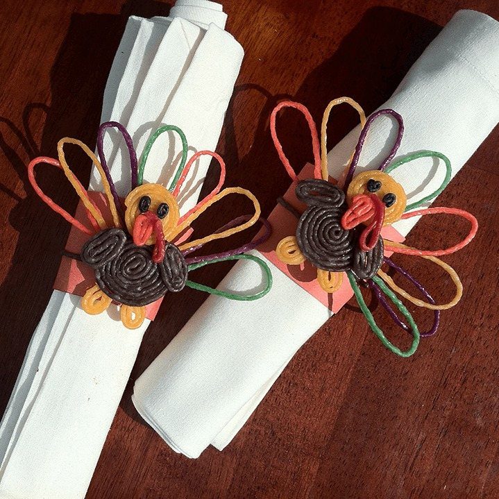Turkey-themed napkin rings with colorful pipe cleaner feathers on white cloth napkins.