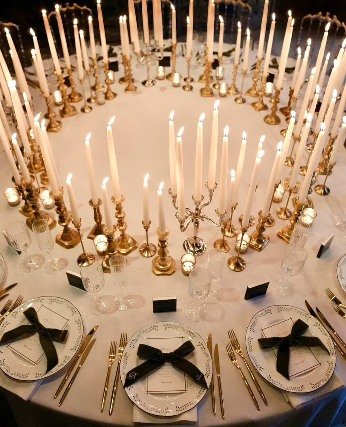 Round table set with white plates and a circle of gold candlesticks.
