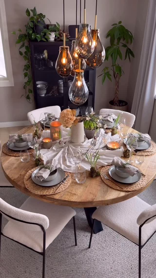Round wooden dining table decorated with autumn greenery, candles, and grey place settings.