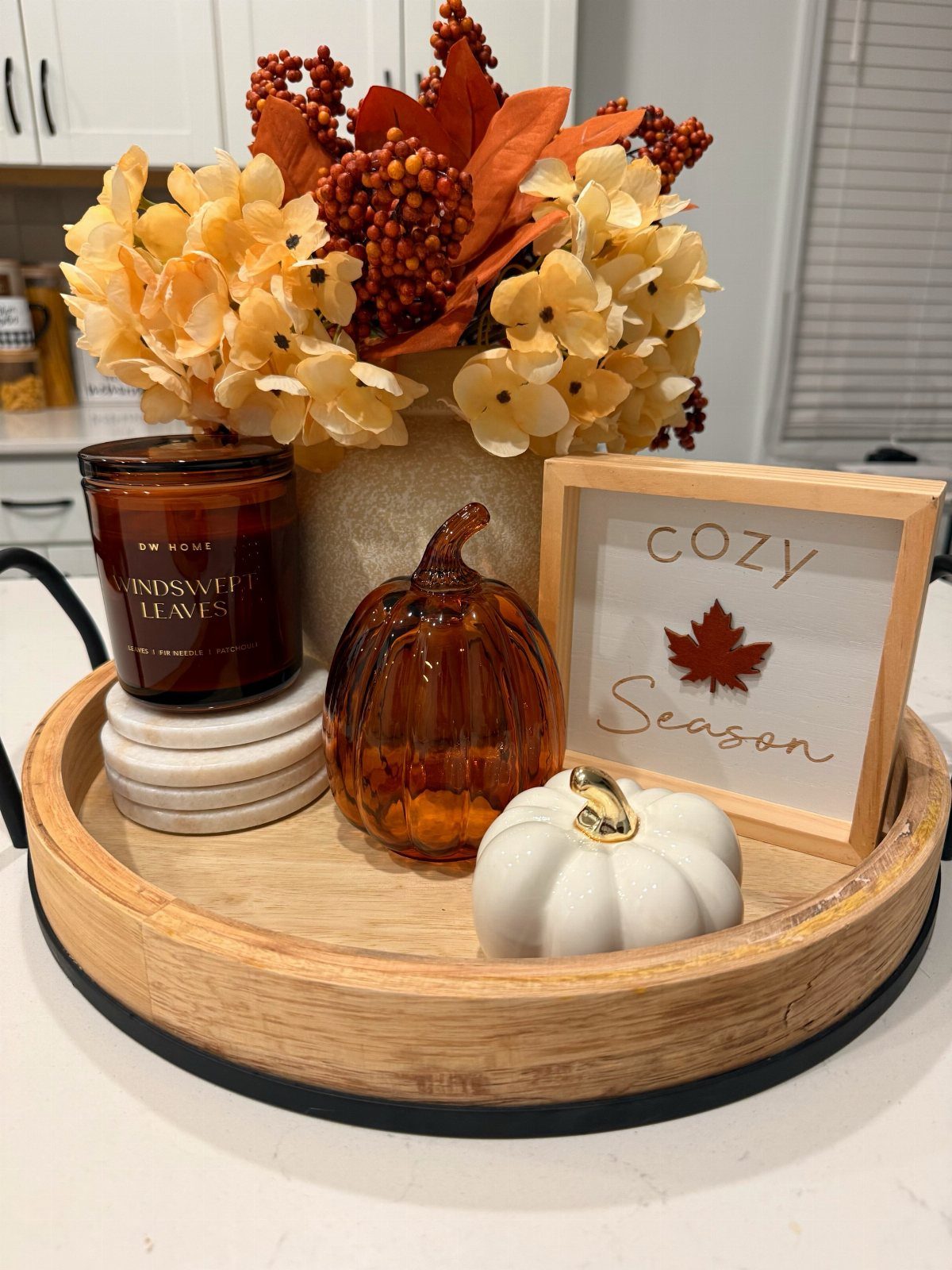 Autumnal table decor featuring pumpkins, flowers, and a candle on a round wooden tray.