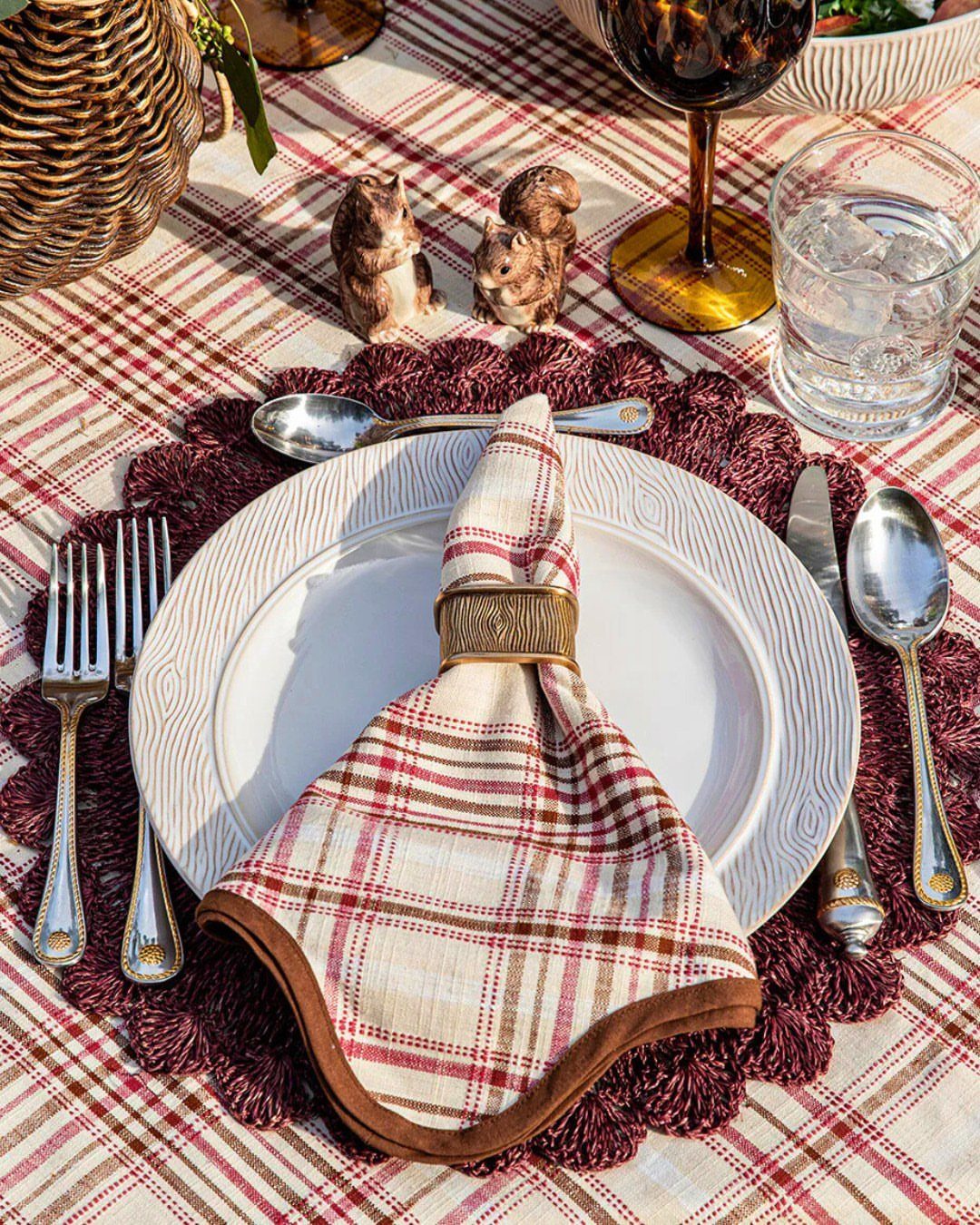 Place setting with plaid linens, gold napkin ring, and silver cutlery on a table.