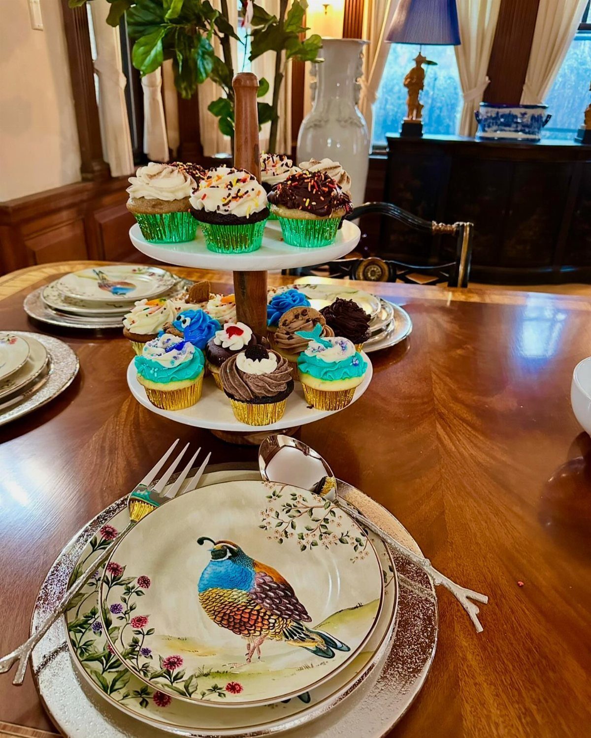 Wooden round table set with pheasant plates and a tiered cupcake stand.