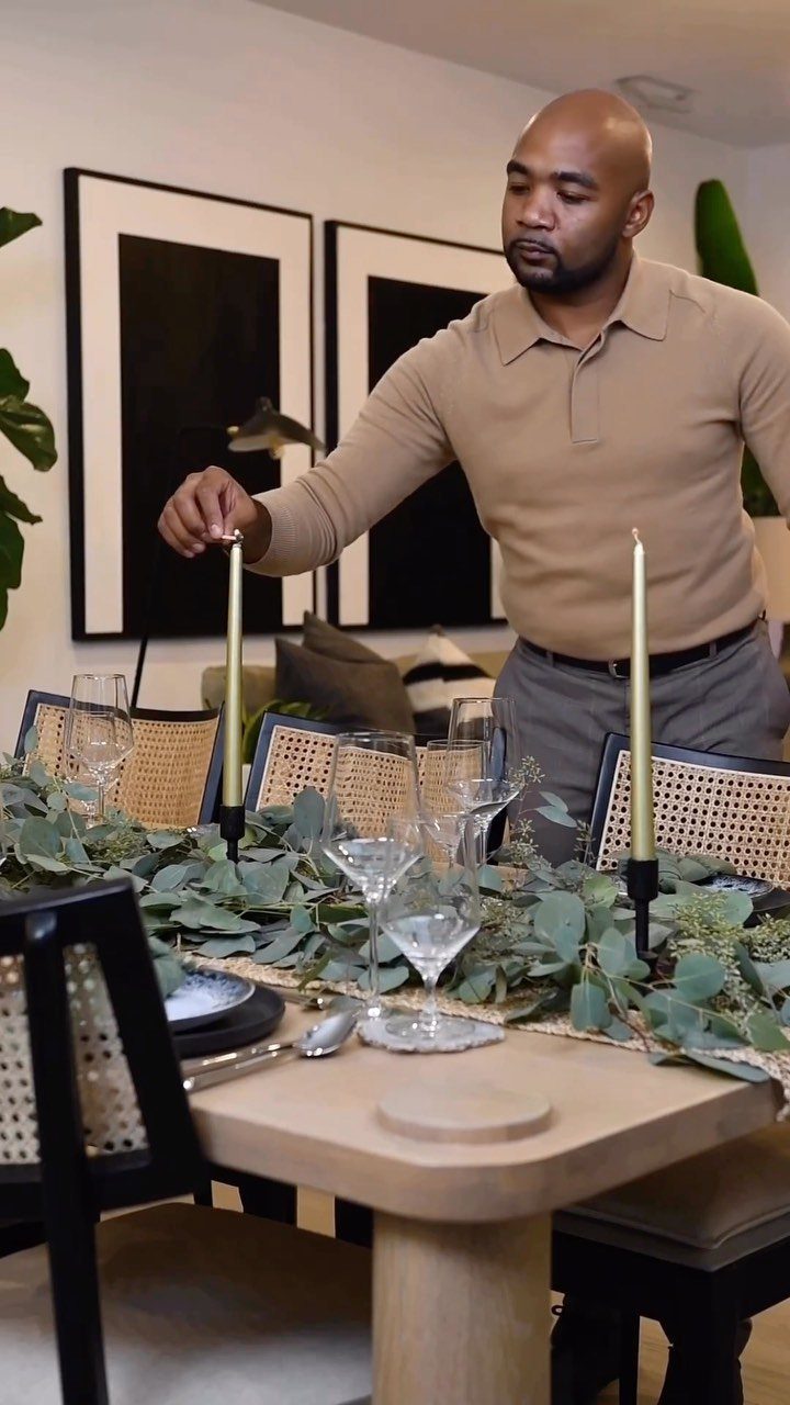 Man adjusting gold candles on a table decorated with a eucalyptus greenery garland.
