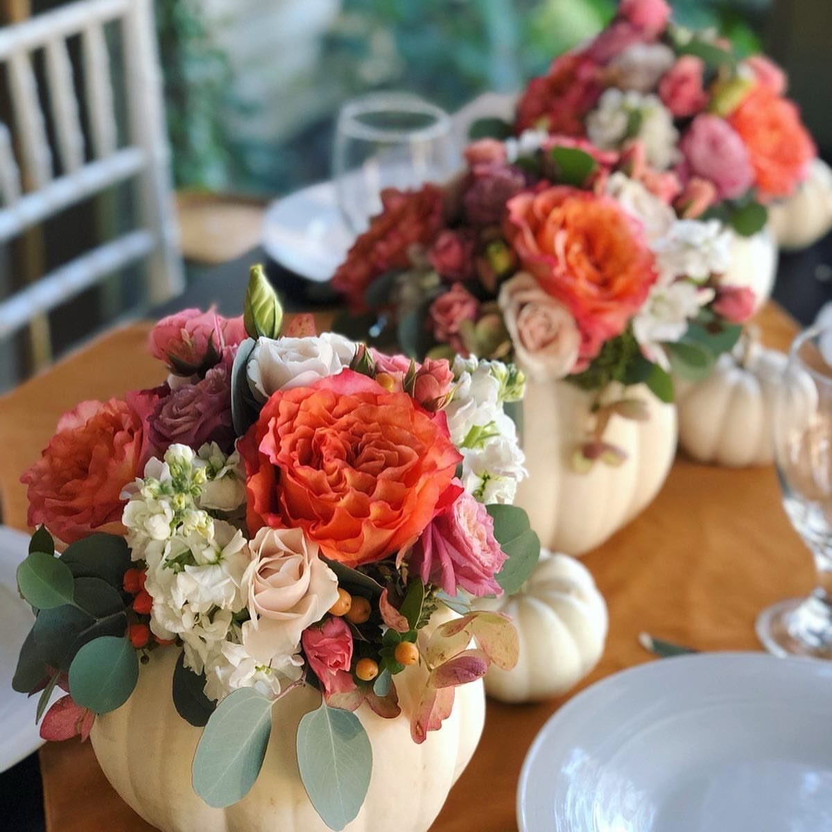 Floral arrangements of orange and pink flowers inside white pumpkins on a wooden table