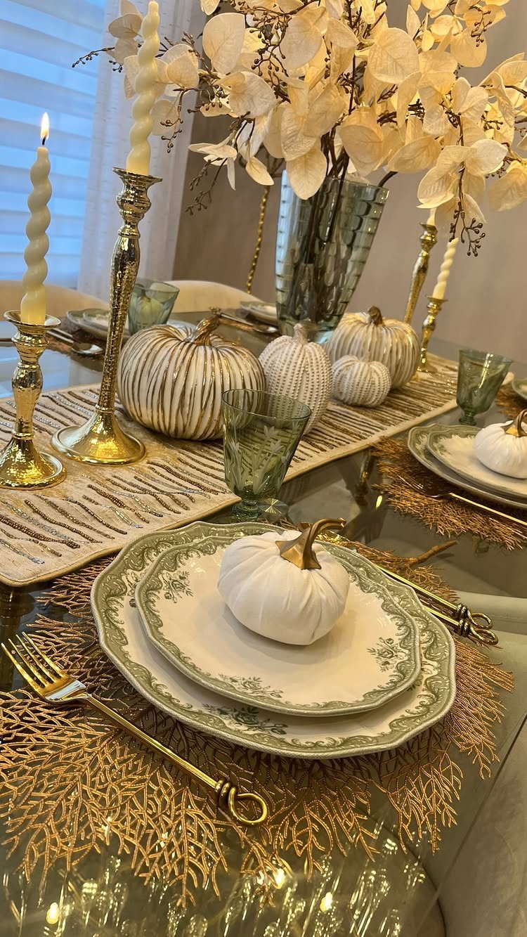 Elegant Thanksgiving table with gold cutlery, white pumpkins, and gold candlesticks on glass.