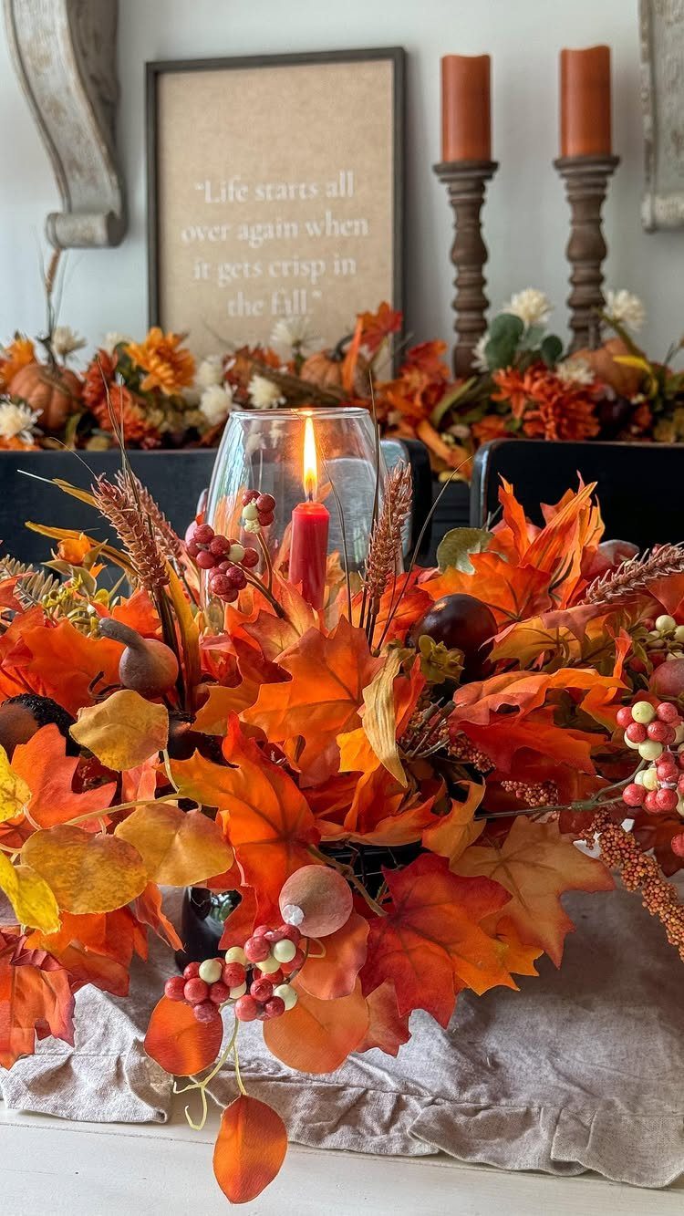 Autumn centerpiece with orange maple leaves, red berries, and a lit candle.