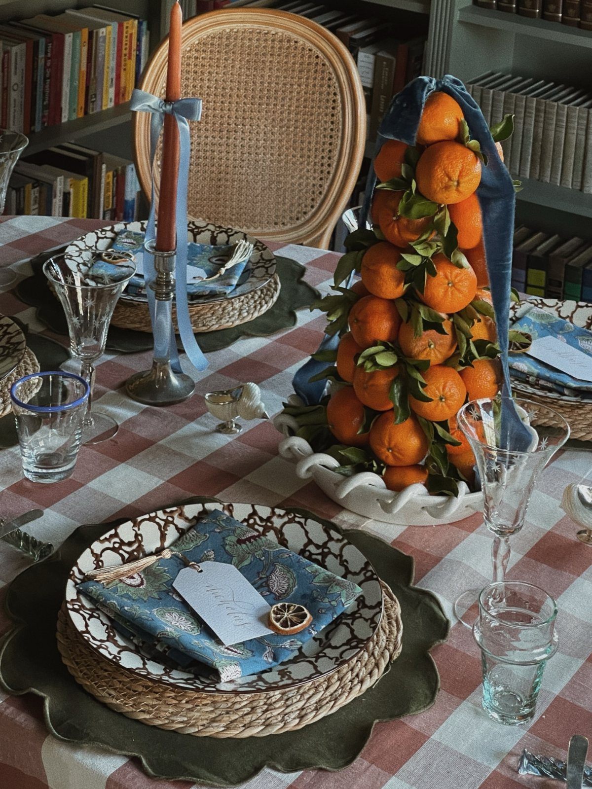 Festive table setting with blue napkins, woven chargers, and a stacked orange centerpiece.