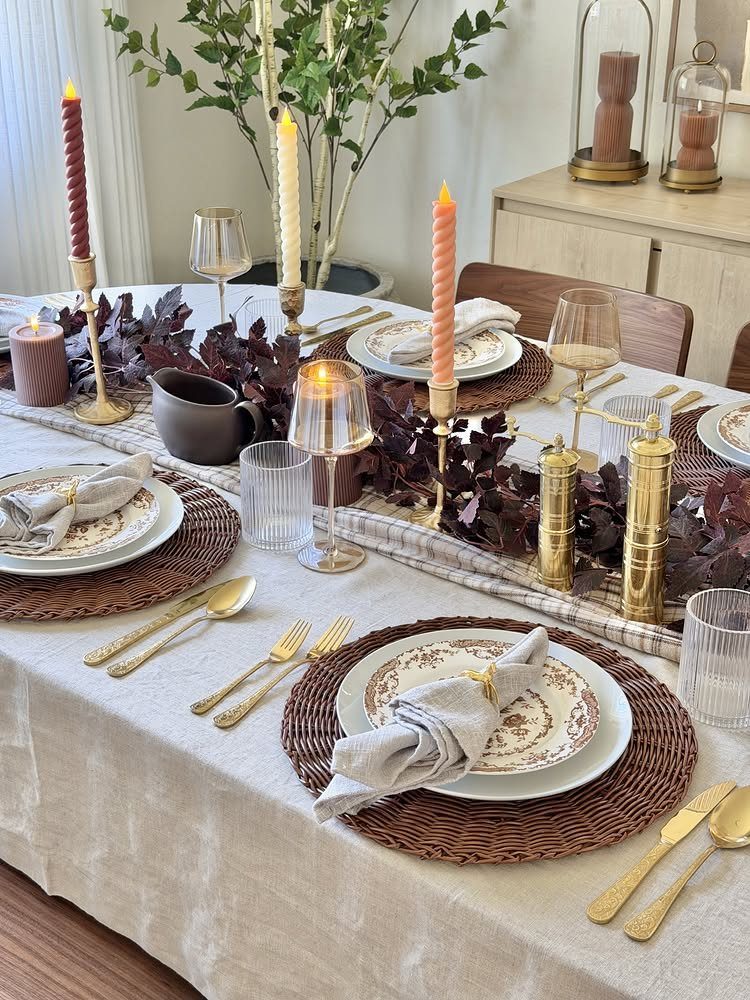 Dining table set with autumn leaves, gold flatware, and orange taper candles.