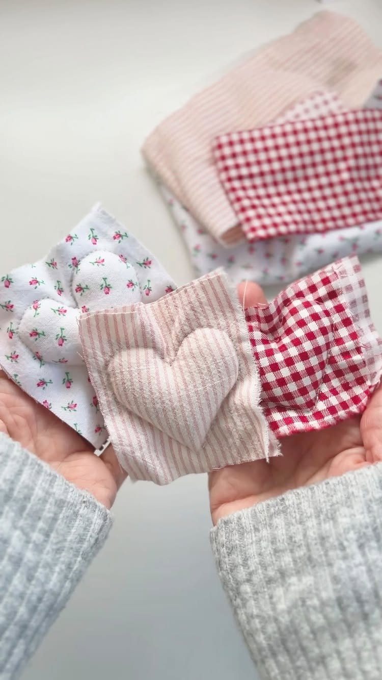 Three small fabric squares with sewn heart pockets held in two hands.