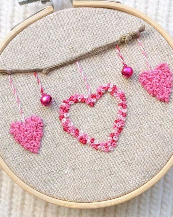 Embroidery hoop with pink stitched hearts and beads hanging from a brown branch.