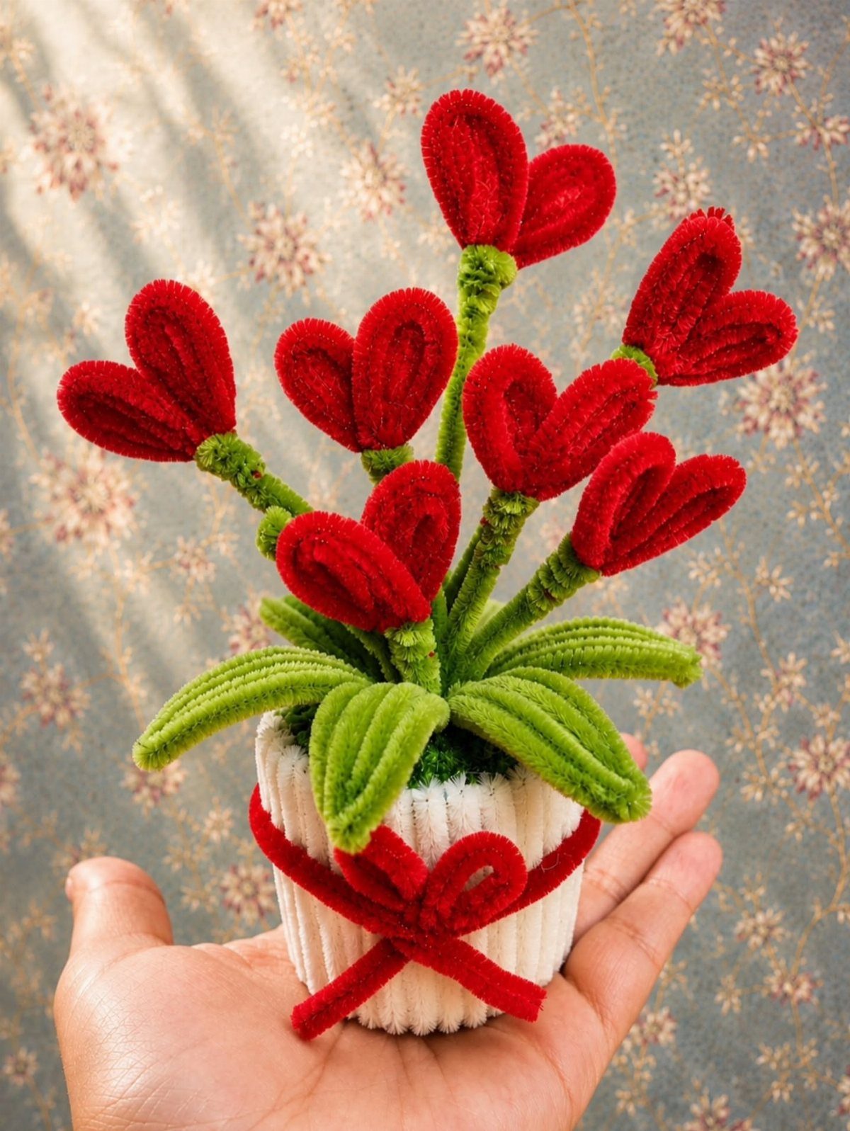 Small white pot with red heart-shaped fuzzy flowers and a red ribbon bow.