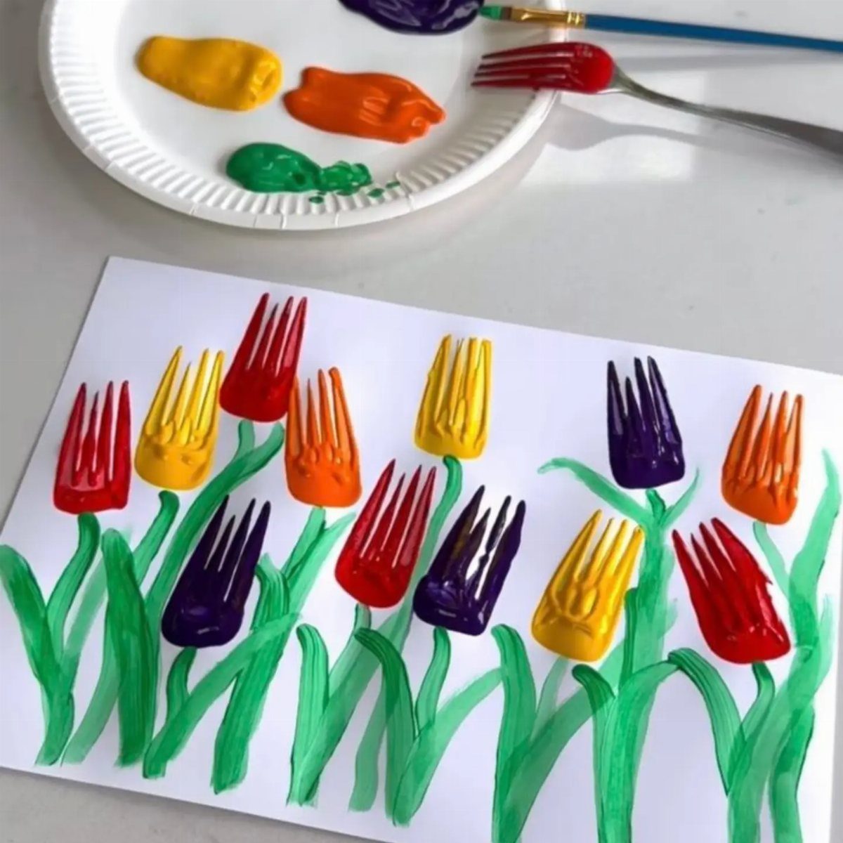 Colorful fork-painted tulips with green stems on a white piece of paper.