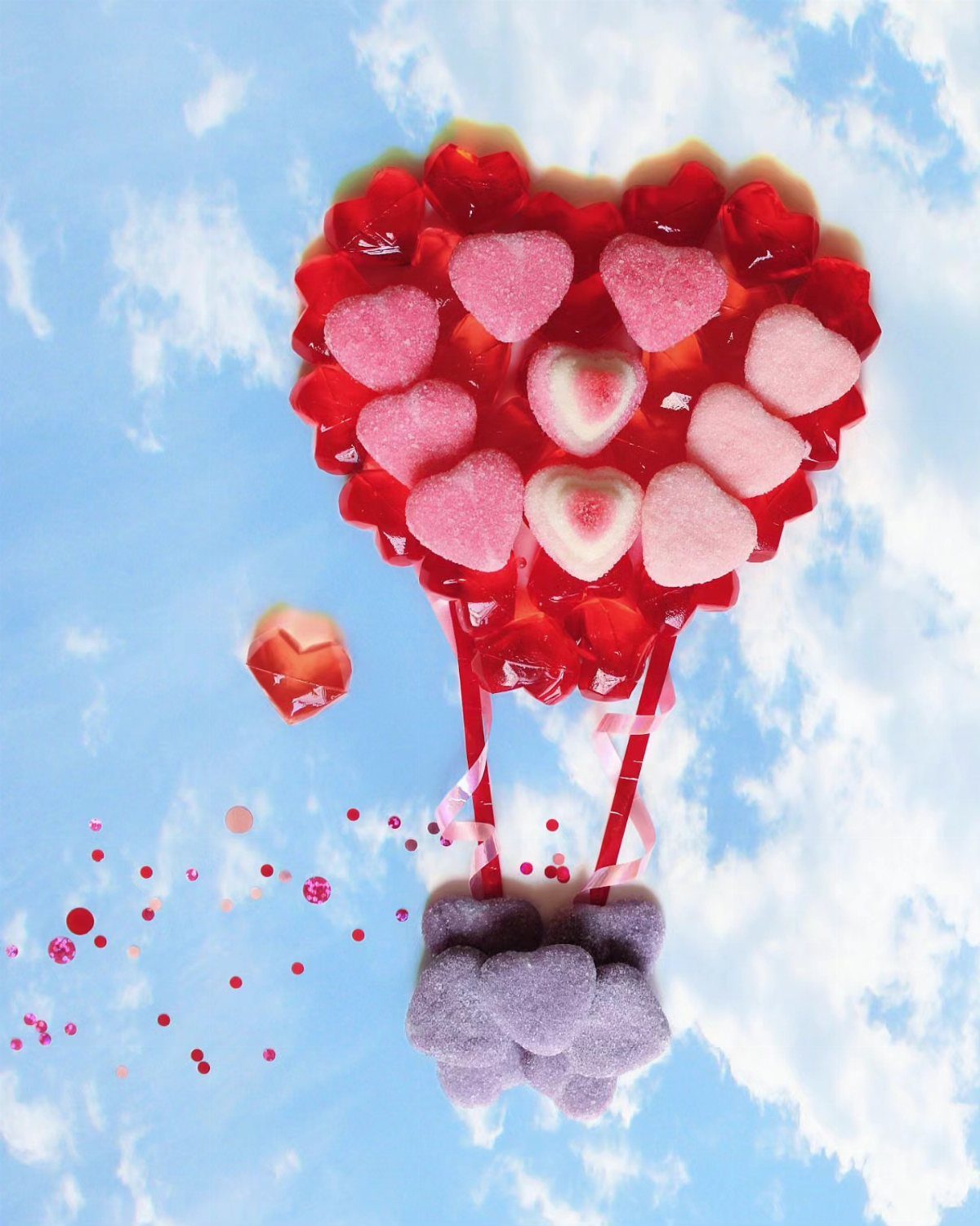 Heart-shaped hot air balloon made from red and pink gummy candies on cloudy sky.