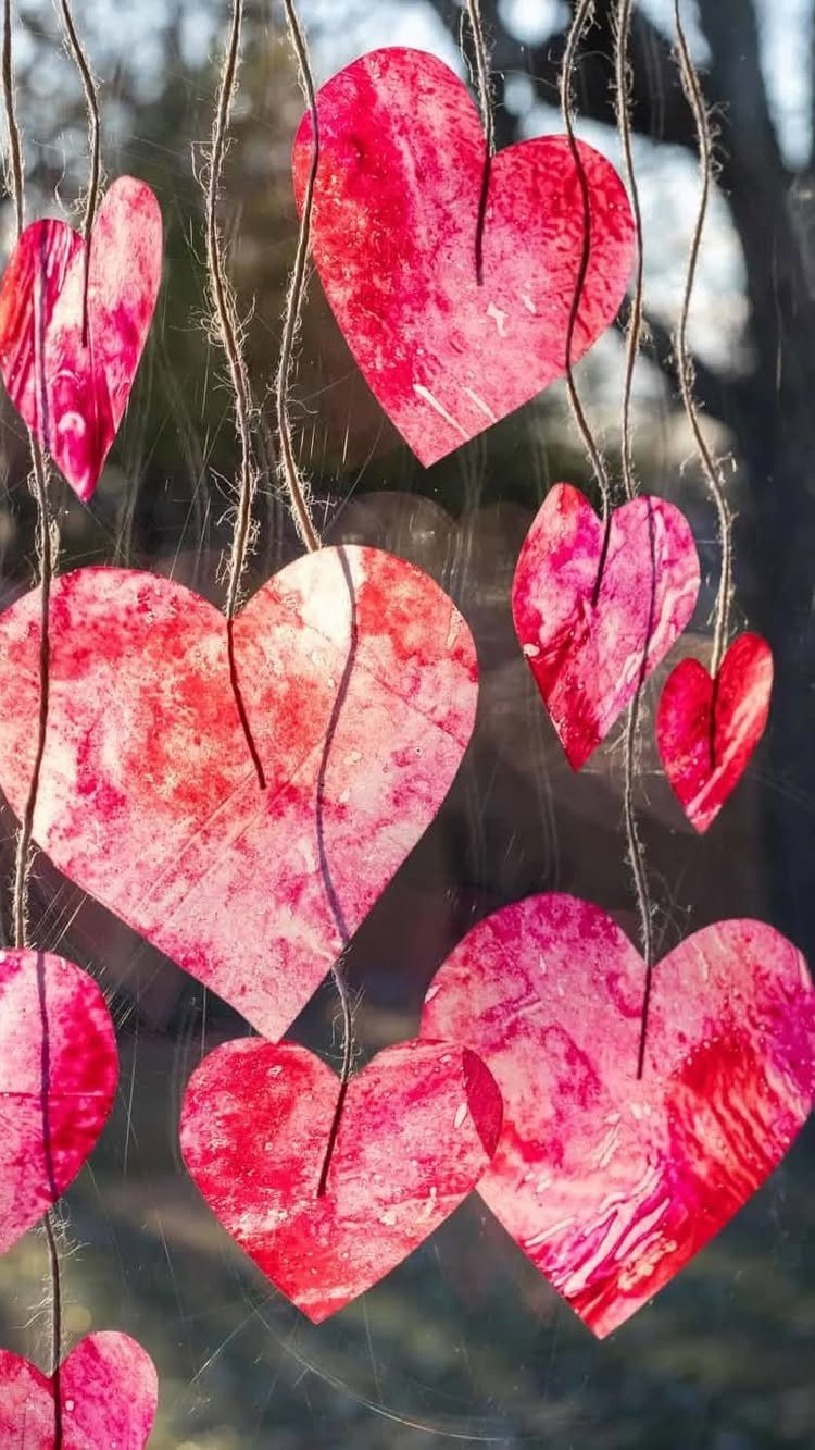 Red and pink marbled paper hearts hanging from strings in an outdoor setting