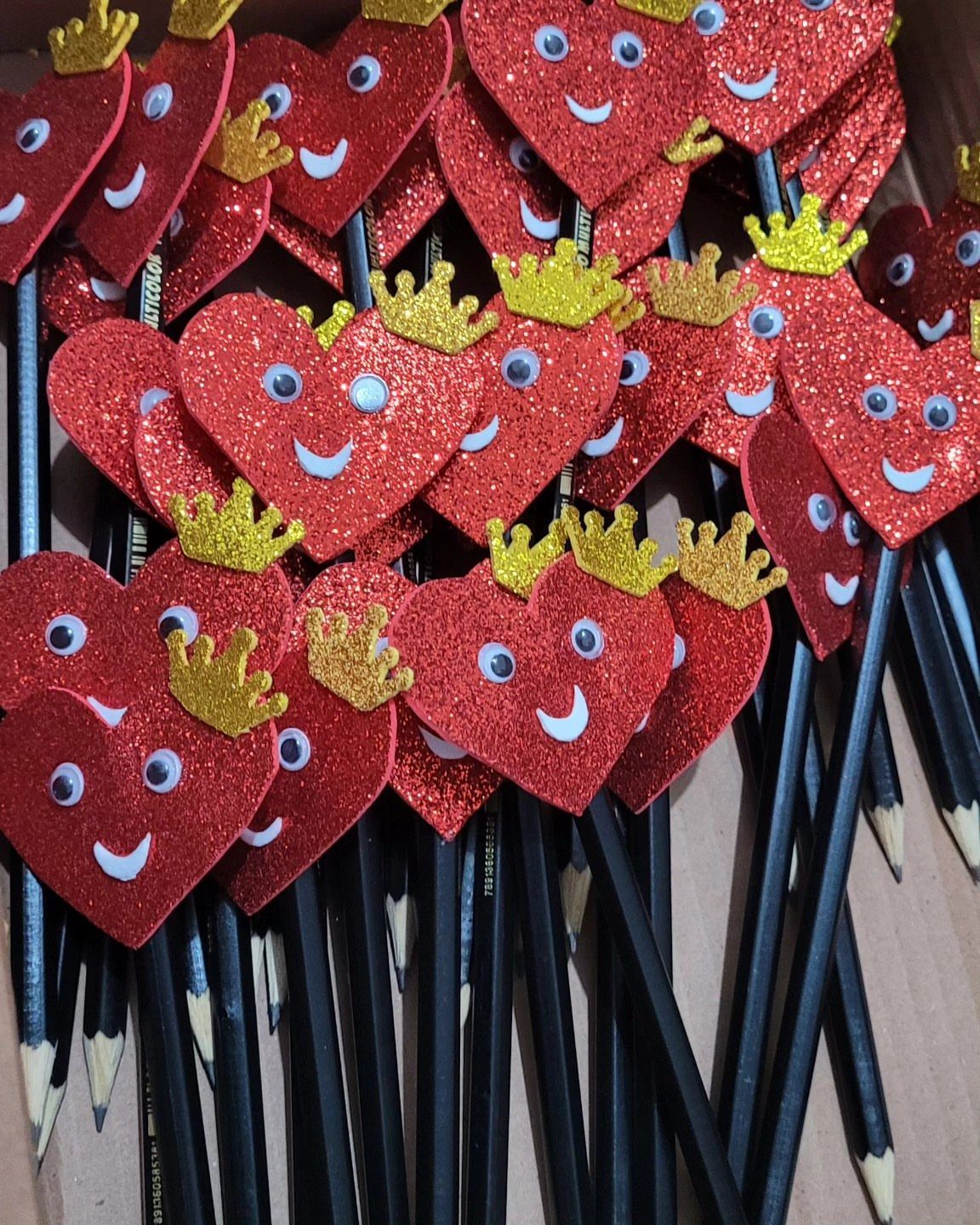 Red glittery heart pencil toppers with googly eyes and gold crowns on black pencils.