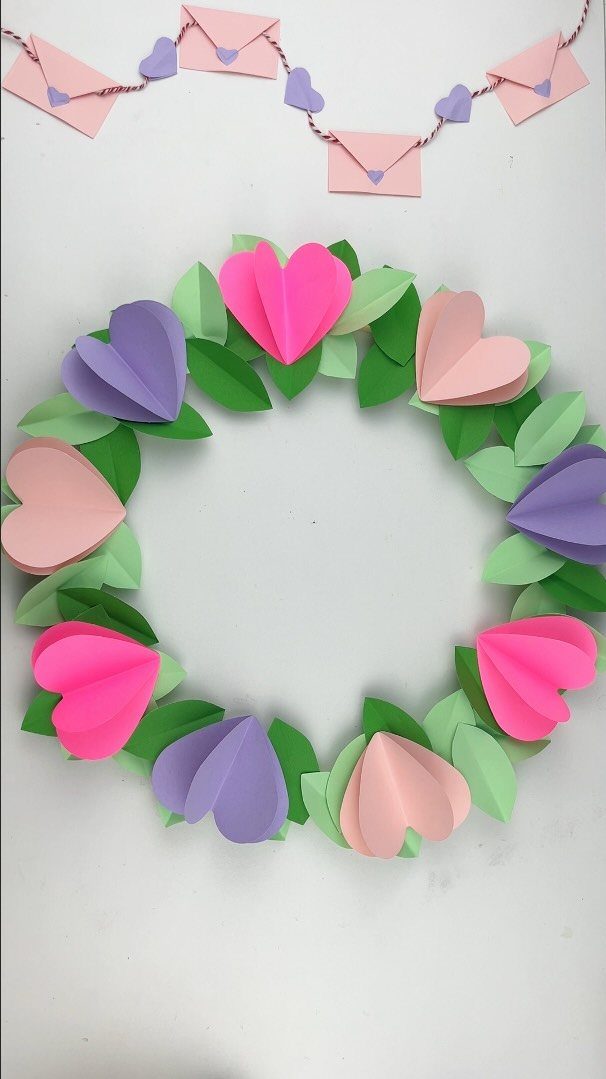 Paper heart wreath with green leaves and a matching envelope garland on white.
