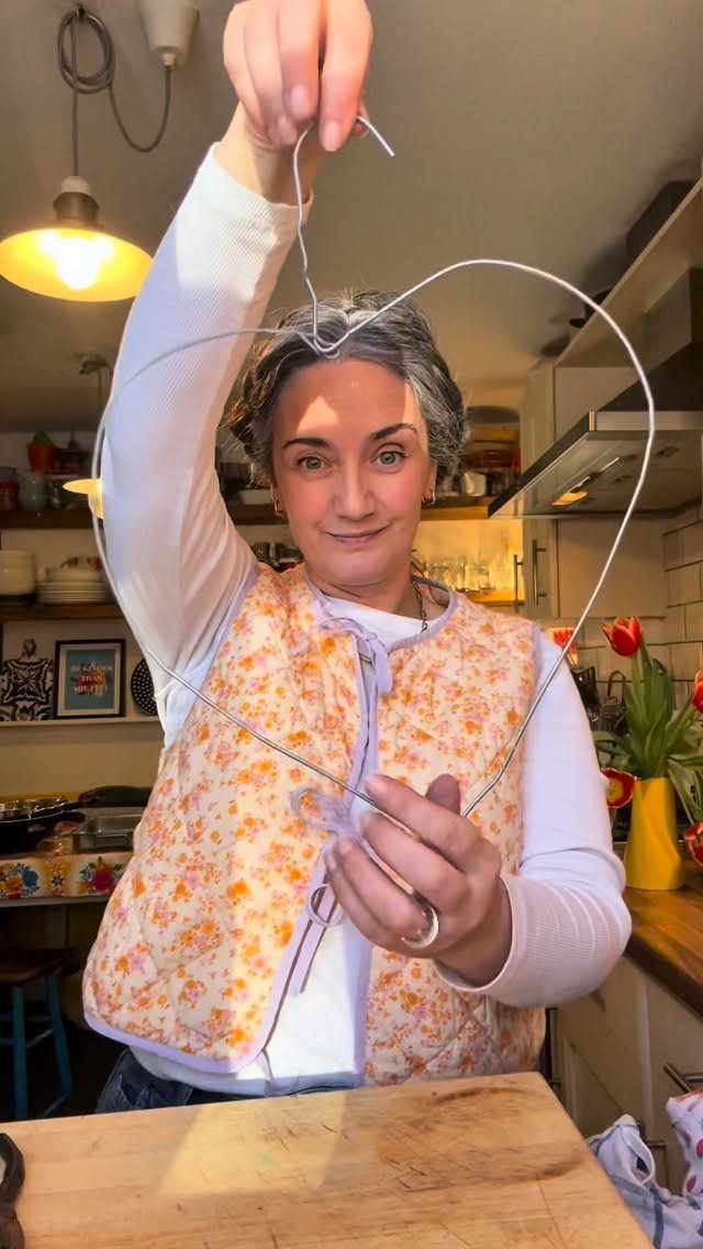Woman holding a heart shape crafted from silver wire in a kitchen setting