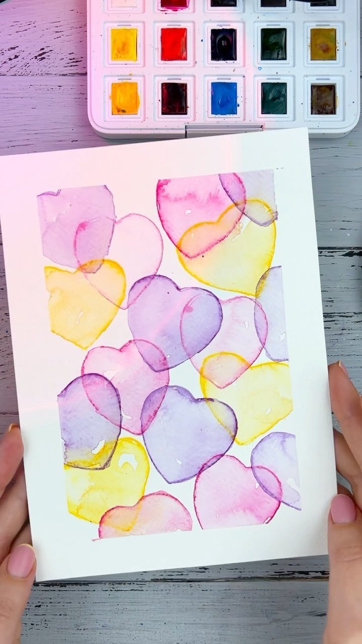 Watercolor card with overlapping pink, purple, and yellow hearts held by hands.
