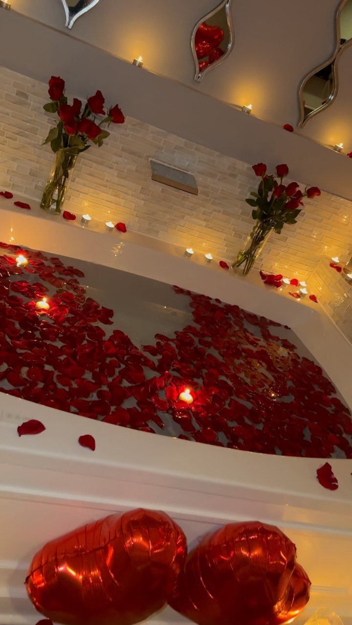 Bathtub filled with red rose petals, candles, red roses, and heart balloons.