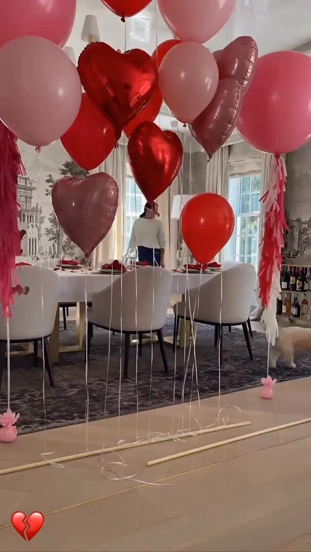 Heart-shaped red and pink balloons floating above a white dining room table setup.