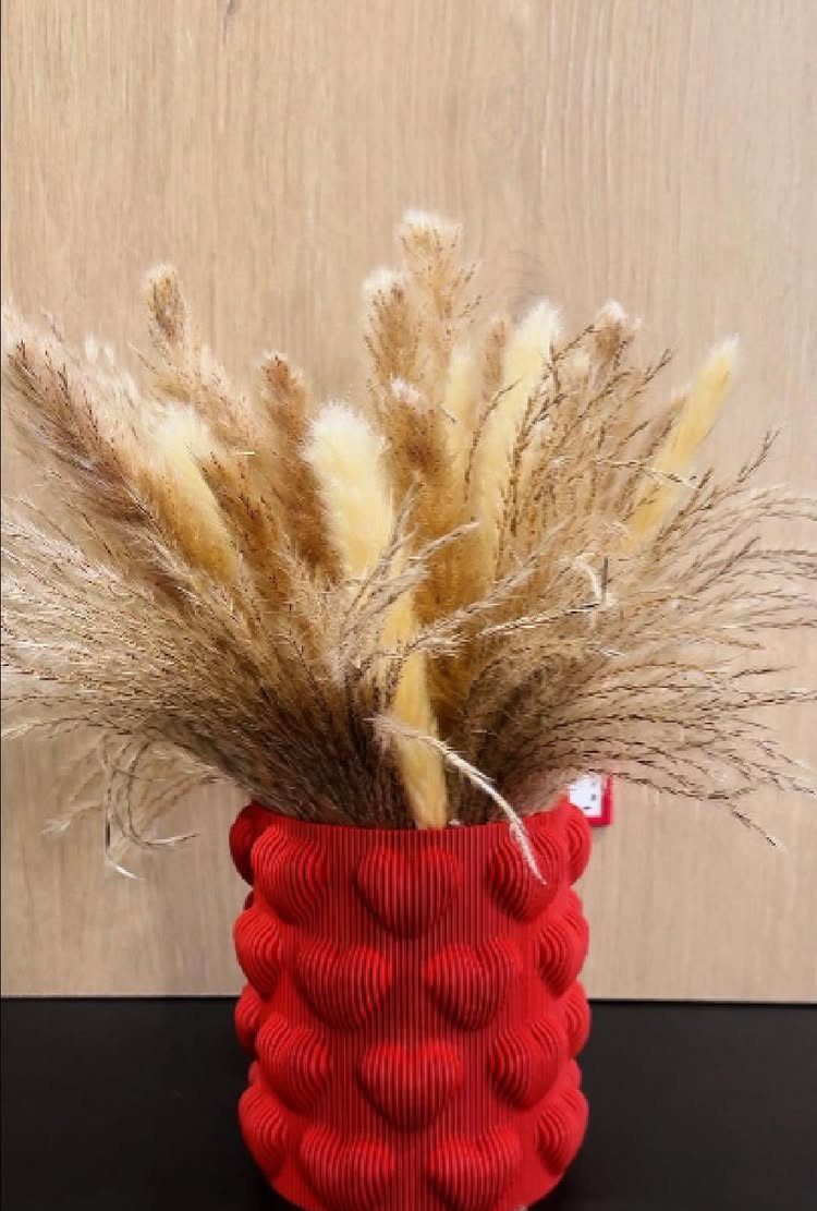 Dried pampas grass in a textured red vase against a wooden wall