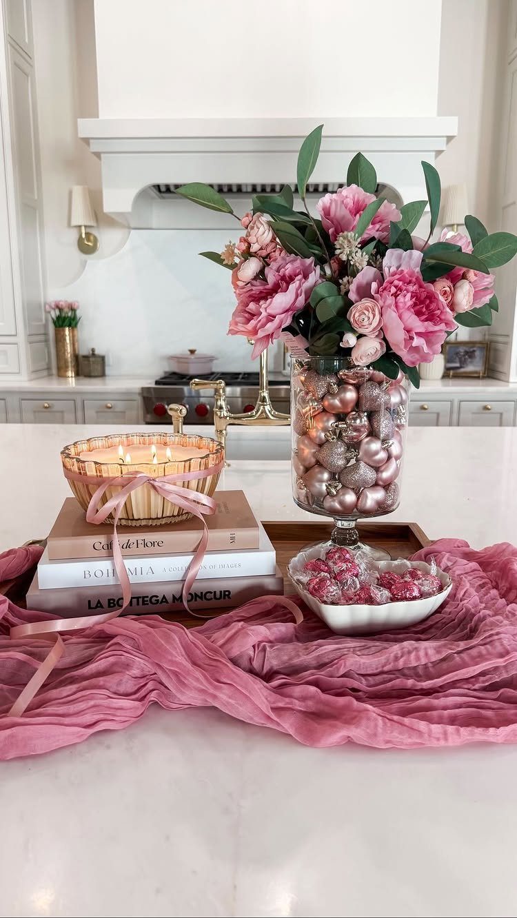Pink peonies and lit candles on a white counter with pink fabric runner.