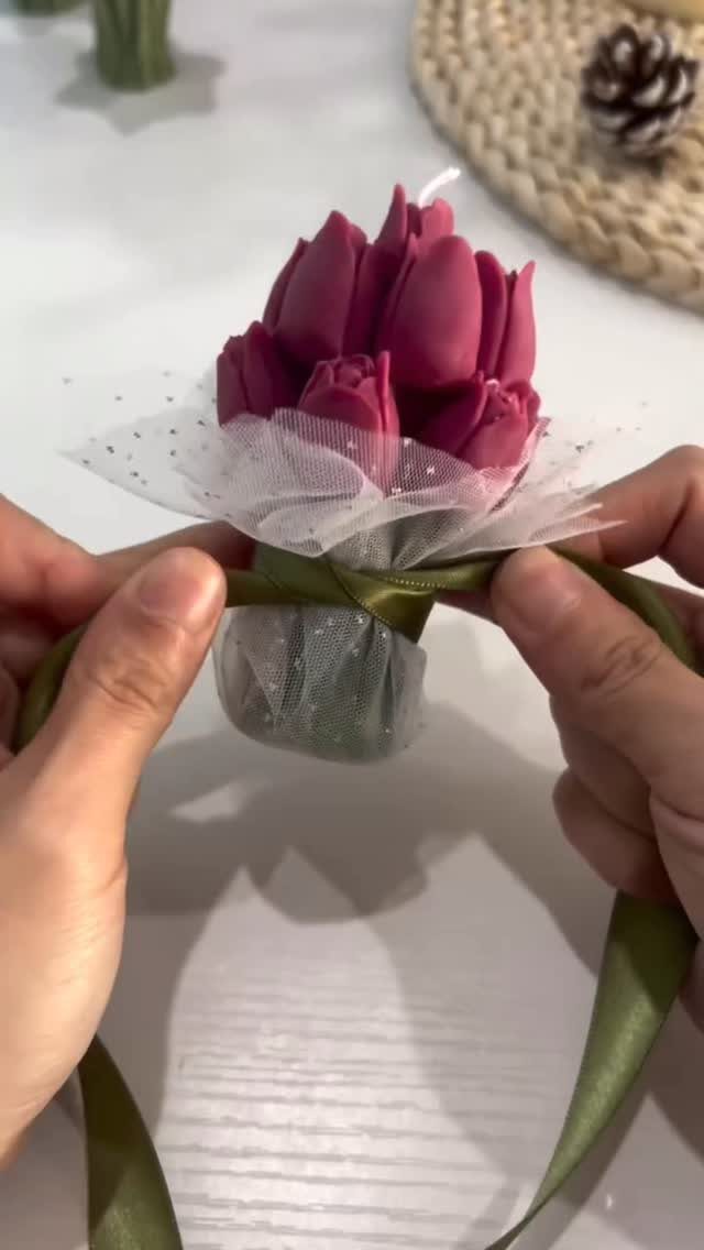 Pink tulip-shaped candle bouquet being tied with a green ribbon by two hands.